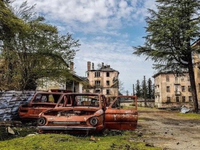 Акармара Ткуарчал — кирпичное здание, заросшее плющом, горы на фоне